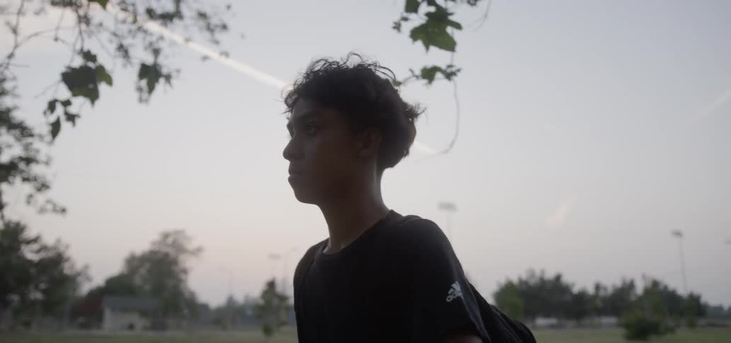 Boy wearing backpack is walking in neighborhood in the evening