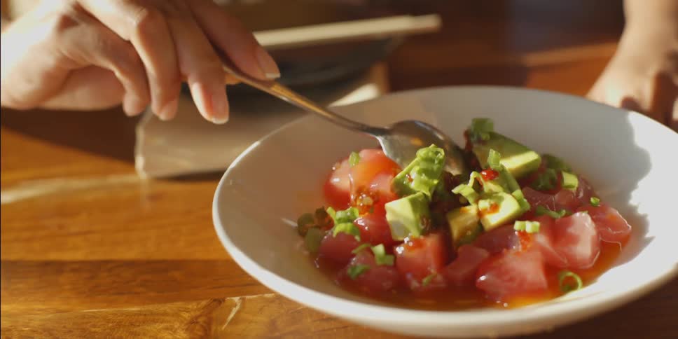 A woman mixes a bowl of tomatoes and avocado