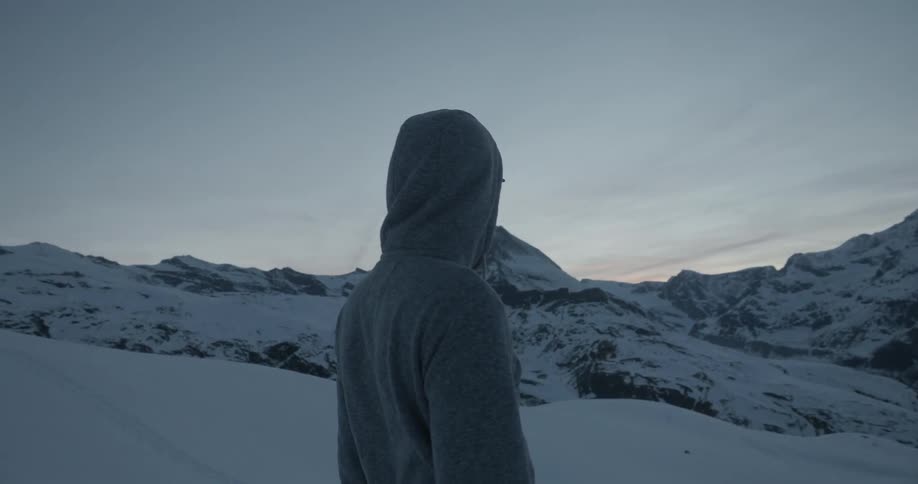 A man stands in a snowy, mountain area and looks up at a peak