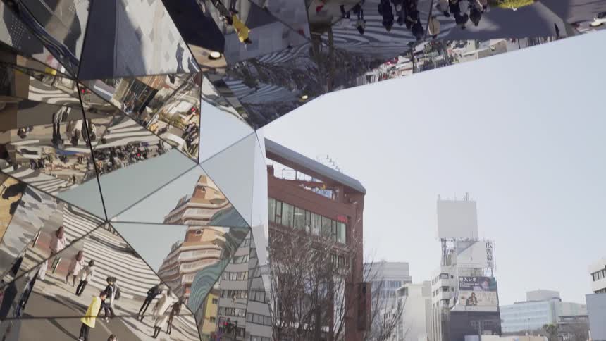 A mirrored structure reflects a busy city street with pedestrians
