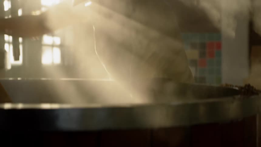 A man is shoveling grains out of a vat inside a brewery in daylight