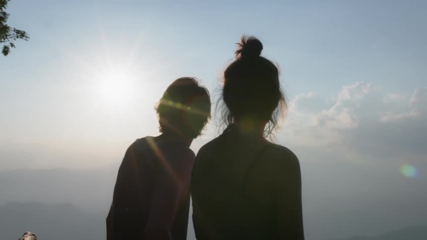 A man and woman sit atop a mountain on a sunny day