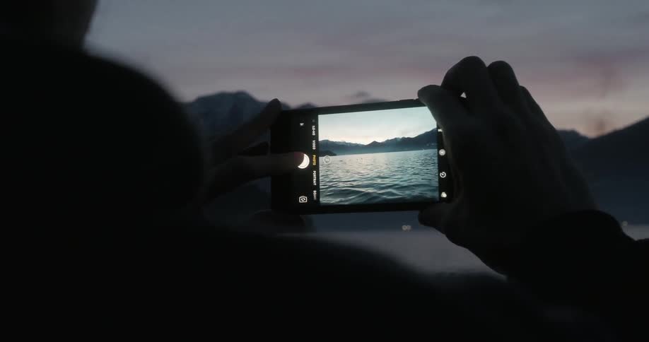 A person is using a cell phone to take photos of a coastal mountain