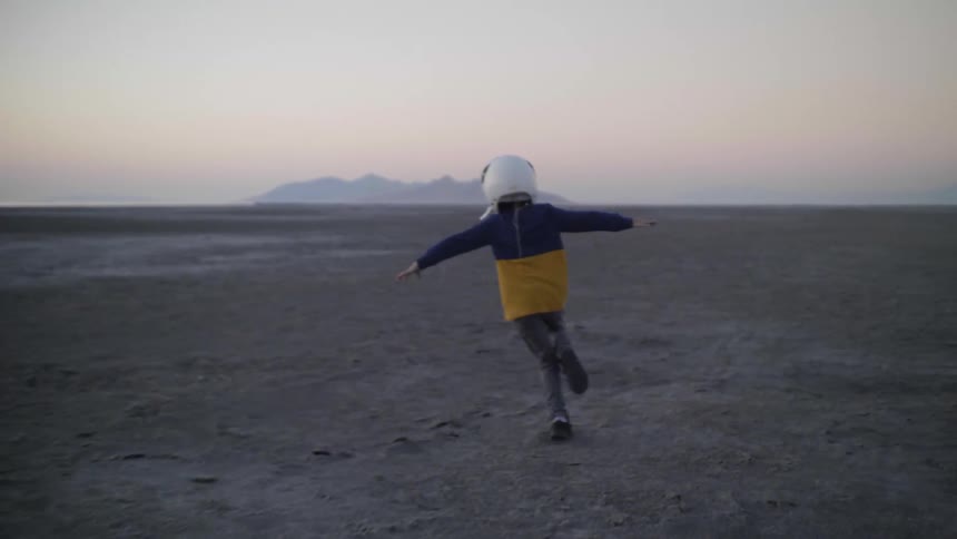 Young child wearing a white aviator helmet pretends to fly across the desert