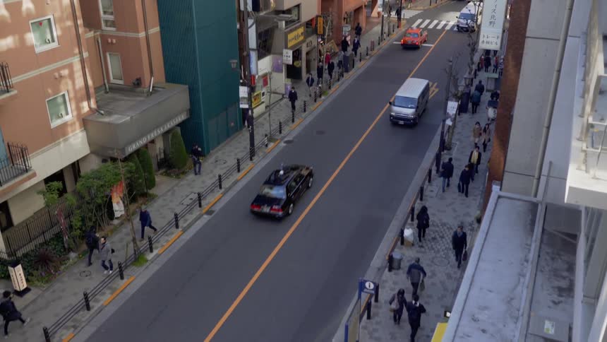 The cars and people walk past the tall buildings below