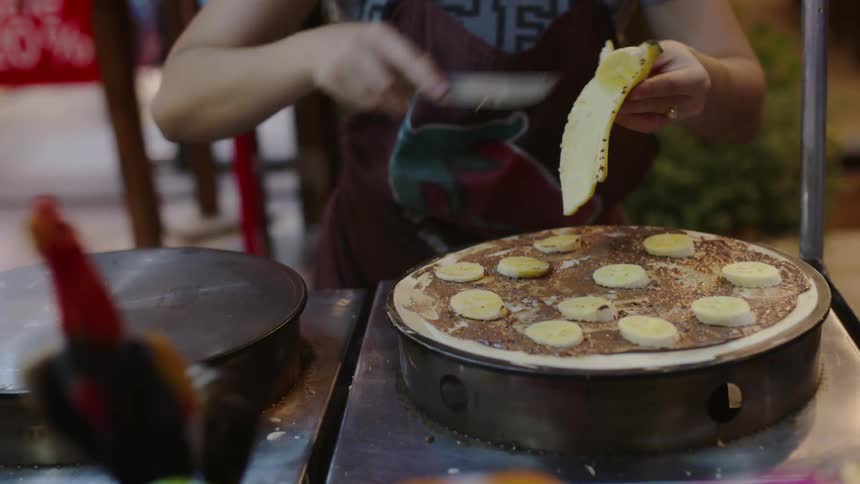 A woman is cutting bananas on some food
