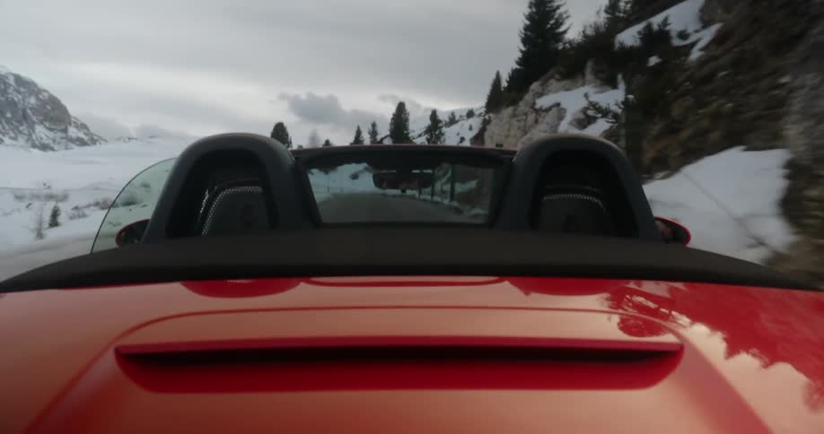 Red sports car convertible driving down a road with snow all around  on a cloudy day