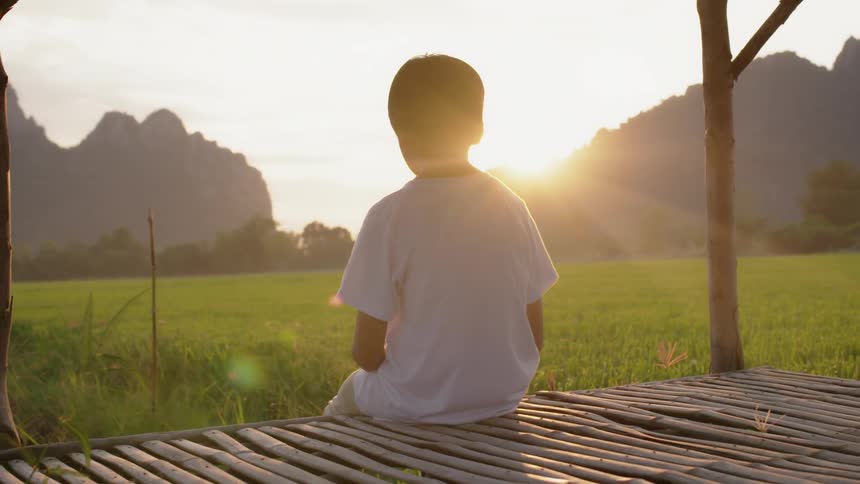 A boy sits on a rural porch at sunset
