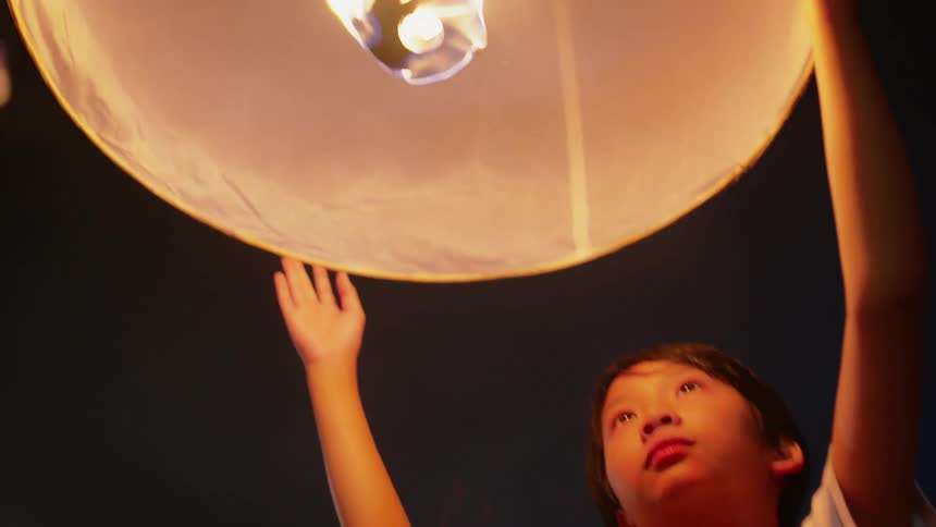 Child holds a lit paper lantern above his head outside at night