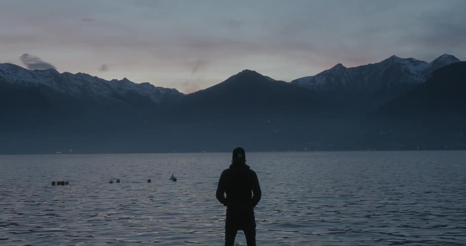 A man stares out over a body of water in front of mountains