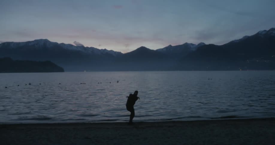 A person skips a stone across a body of water at dusk