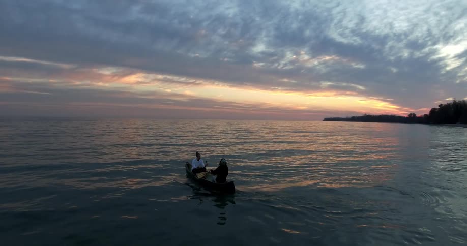 Two people are going out to sea in a canoe at dusk or dawn