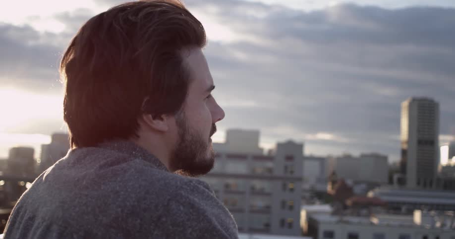 A man with a beard looks out at the city skyline during the day