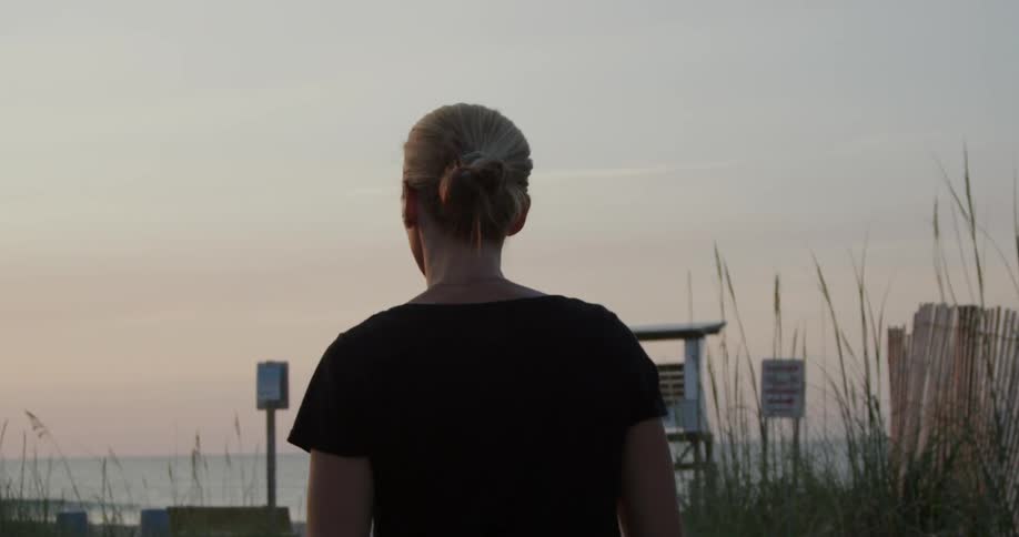 A woman is walking towards the beach at dusk