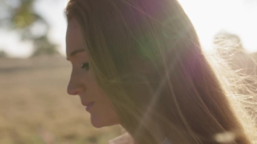 Woman stands in the sun dragging a weed across her face