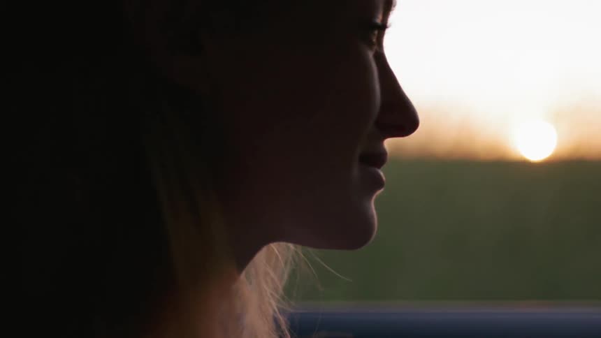 A woman rides in a car by a grass field