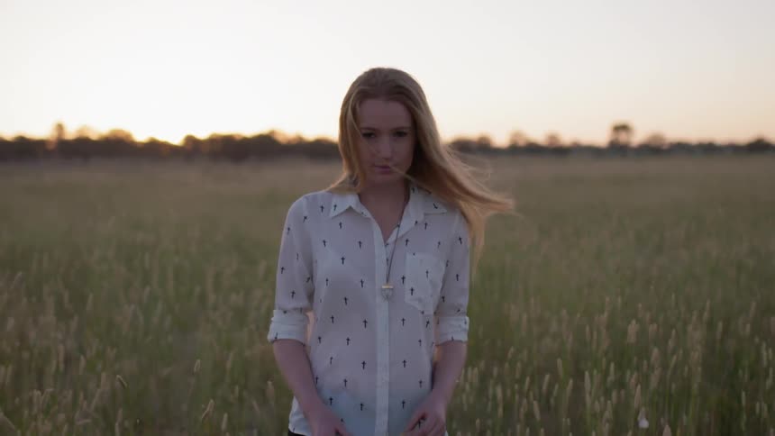 Woman is walking through field of weeds on windy day at sunset