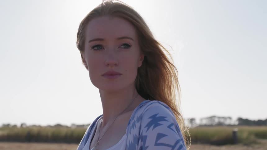 Woman stands in a field as the wind blows her hair