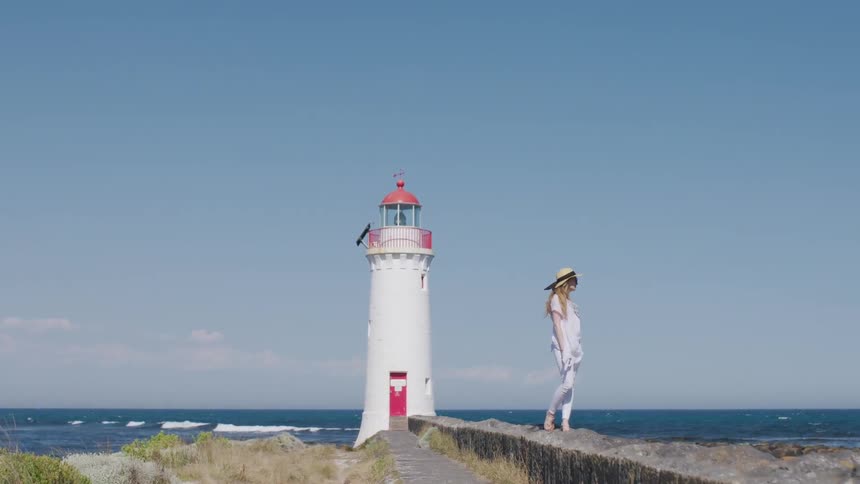 A woman stands by the lighthouse on a windy day