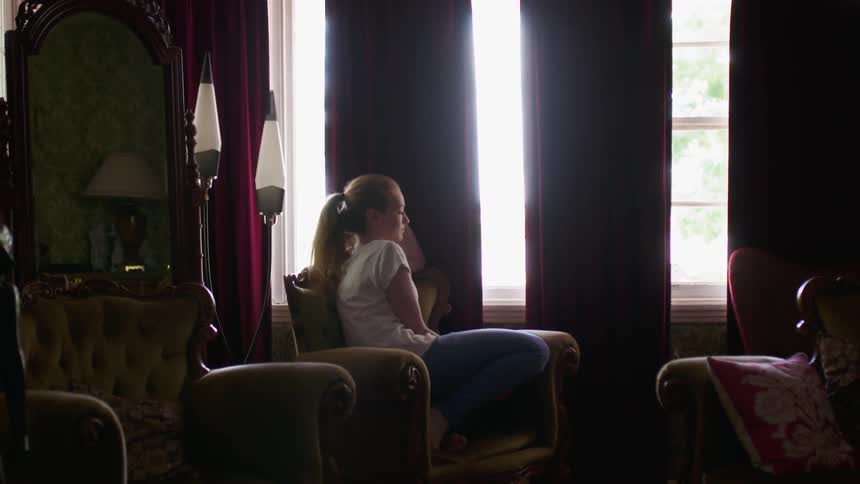 A woman walks into the living room and sits by the window