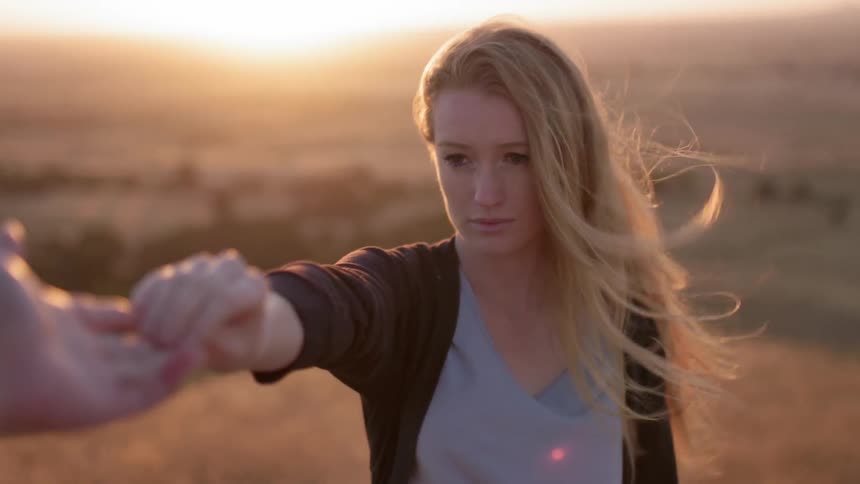 A woman lets go of someone's hand on a windy field