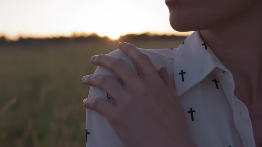 A woman stands in a rural field at sunset