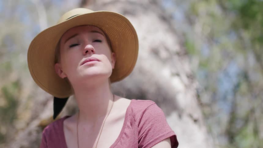 Woman wearing hat is sitting by tree on sunny day