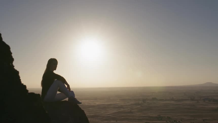 A woman sits on a rock ledge on a sunny day