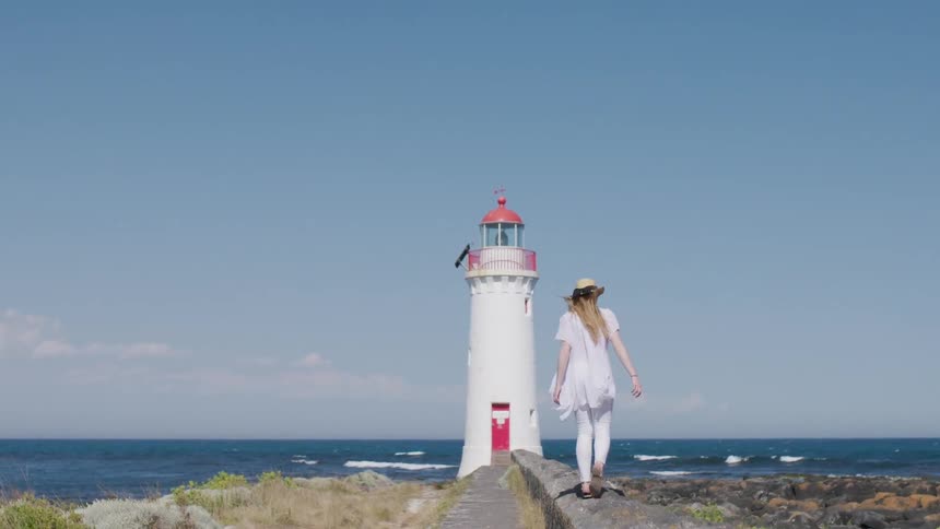 A woman walks towards a lighthouse on a beach