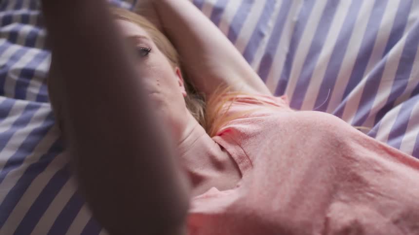 A woman rests in bed waving something in the air
