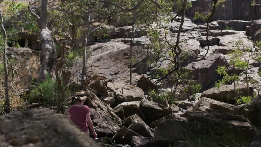 Woman wearing hat is hiking through rocks in wilderness