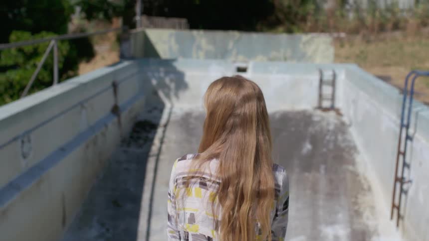 A woman stands by an empty pool