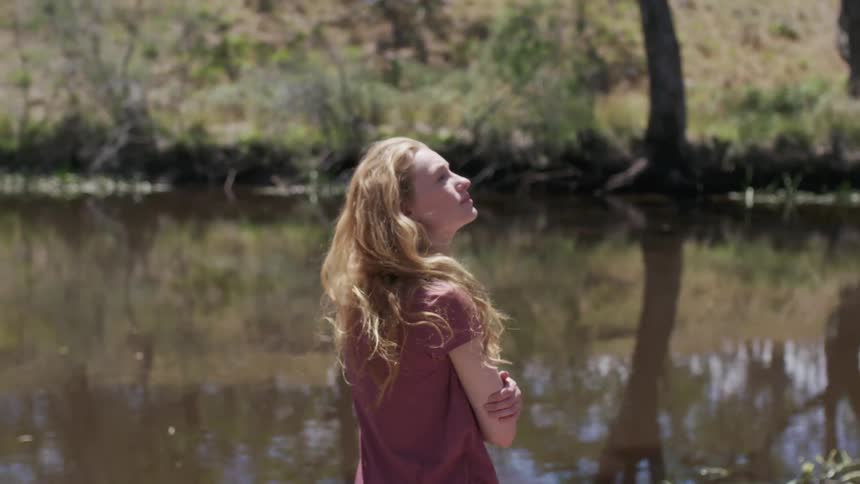 A woman stands next to a rural river on a sunny day