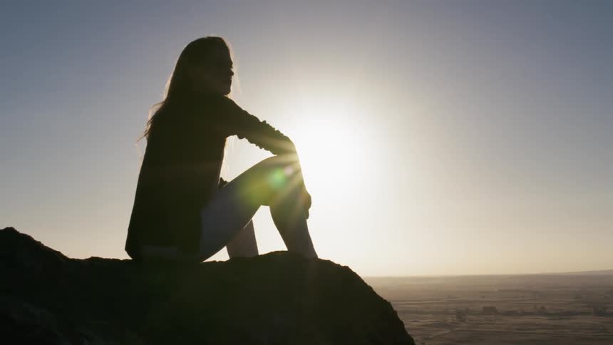 A woman sits overlooking a valley at sunset