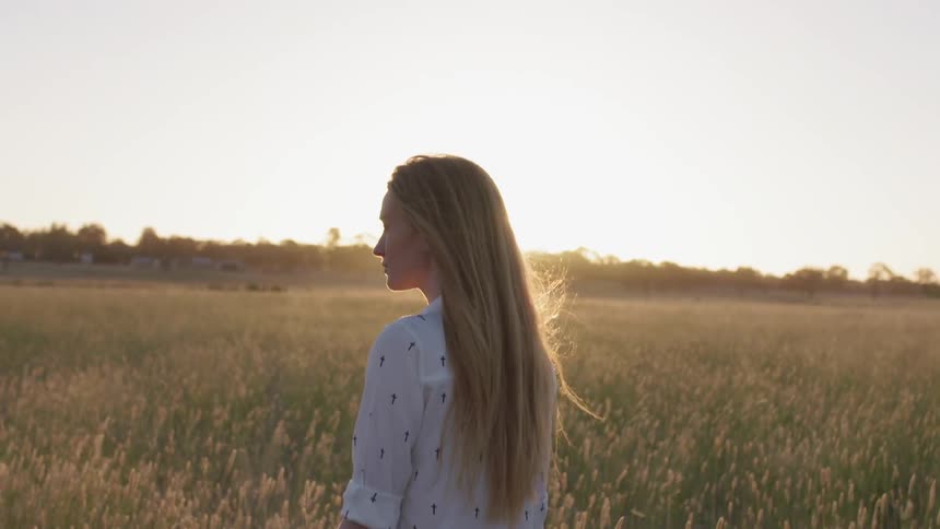 Long-haired blond walking through a golden field at sunset
