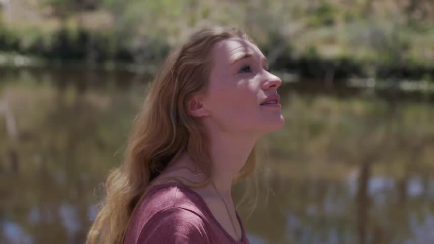 A woman stands next to a rural river