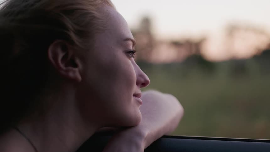 A woman leans out the window of the moving car