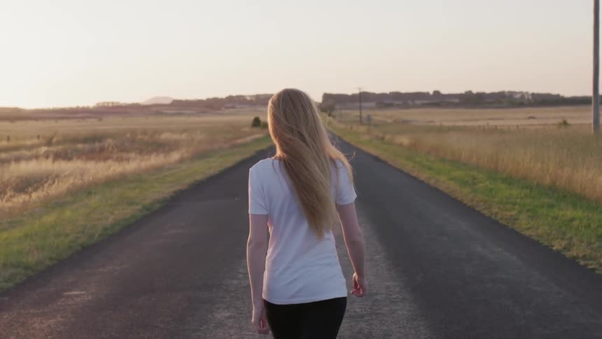 A woman walks on a rural road at sunset