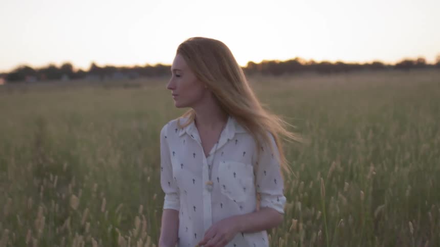 Woman is walking in field at sunset on windy evening