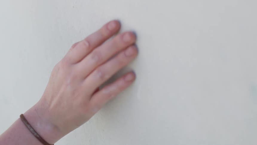A person drags their hand along a wall as they walk by