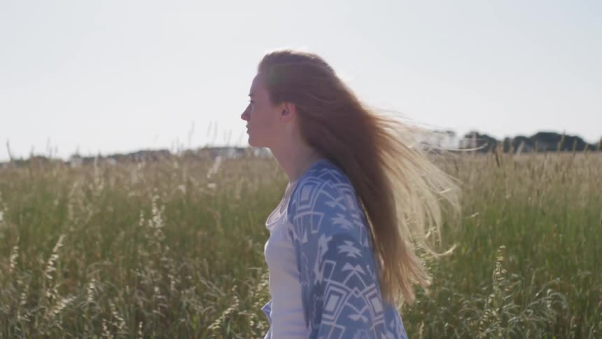 A woman walks in a field with tall grass