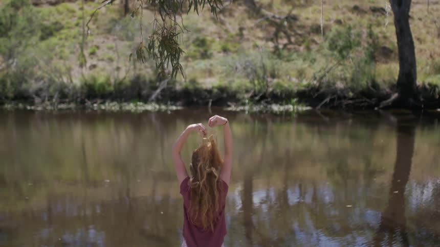 Girl standing in front of a lake stretching in the afternoon