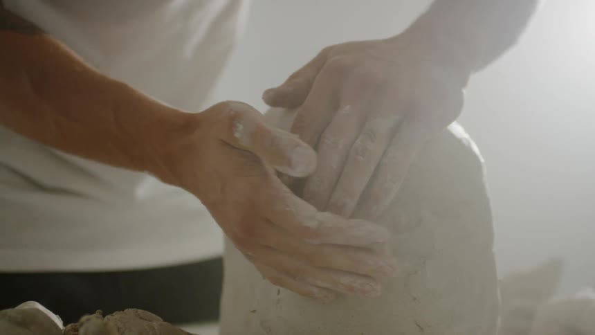 An artisan is forming clay inside in daylight