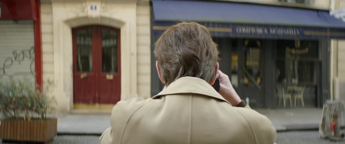 A man is photographing another man as he walks down a city street in daylight