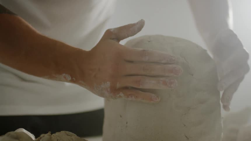 An artisan is forming clay inside in daylight