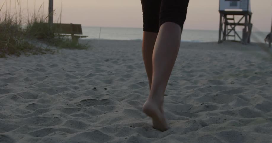 A man walking through the sand towards a lifeguard shack and the beachfront