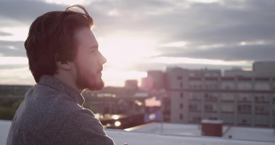 Man stands enjoying the breeze and view atop a city building