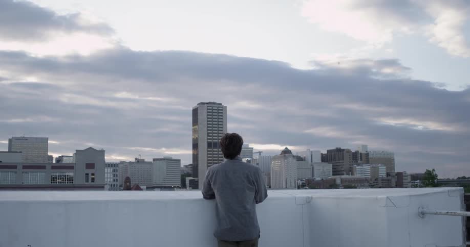 A man stands at a ledge and looks at the city in the morning