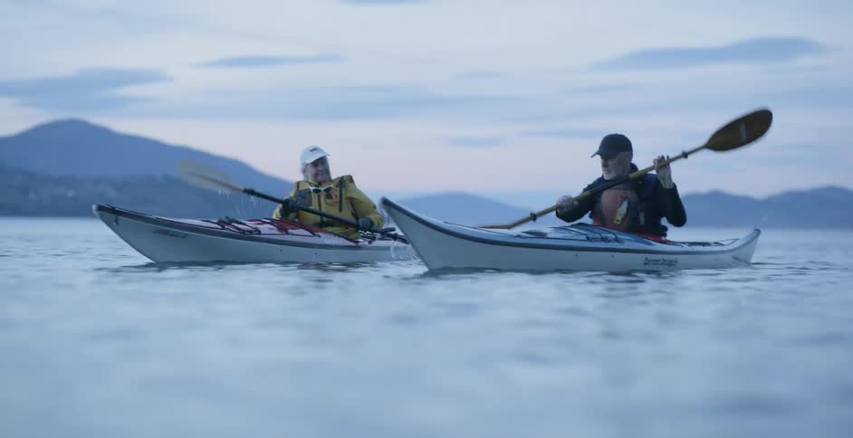 A man and woman row kayaks through the water at sunset
