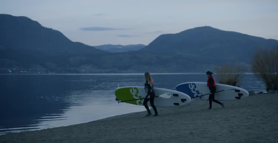 Two women carry their paddle boards and oars to the water